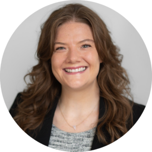 Woman with long brown hair smiles at the camera. She is wearing a black blazer over a grey patterned top against a plain light background, embodying the confidence and determination seen in 2024 PBPH Success Stories.