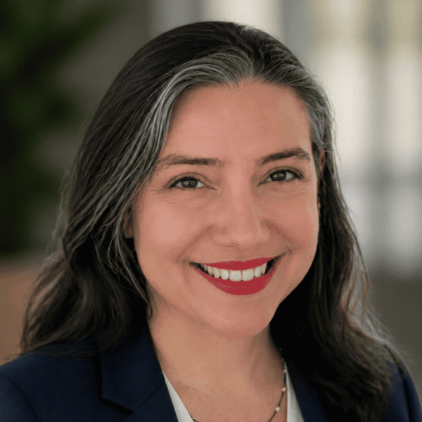 A woman with dark hair featuring silver streaks smiles while wearing a navy blazer and white top.